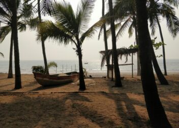 Serene beach setting in Alibag with palm trees and a wooden boat basking in the sunset.