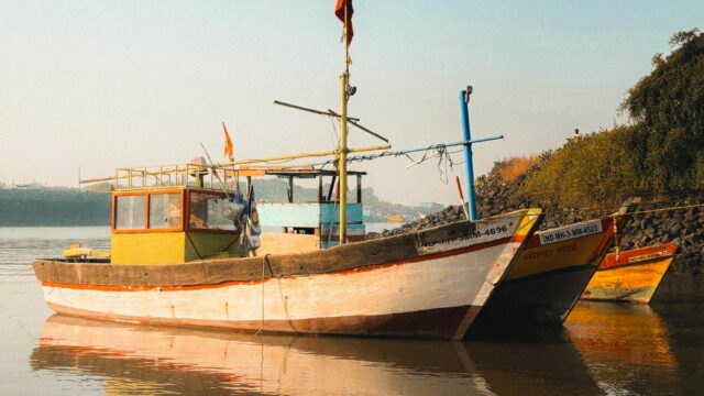 Traditional fishing boats anchored at Alibag harbor with a peaceful water reflection.